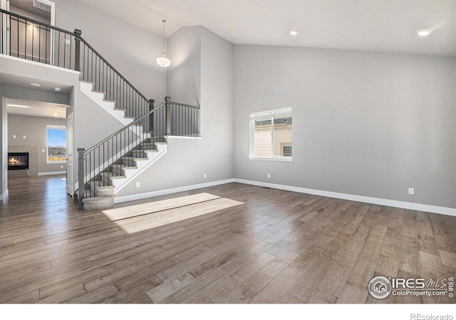 unfurnished living room featuring a fireplace, wood-type flooring, and high vaulted ceiling