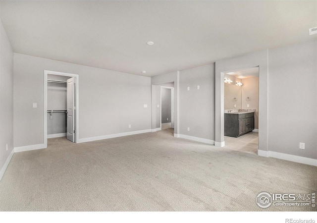 unfurnished bedroom with a closet, light colored carpet, a spacious closet, and ensuite bath