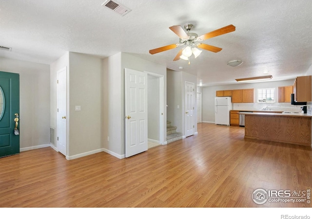 kitchen featuring backsplash, white refrigerator, light hardwood / wood-style flooring, ceiling fan, and a textured ceiling