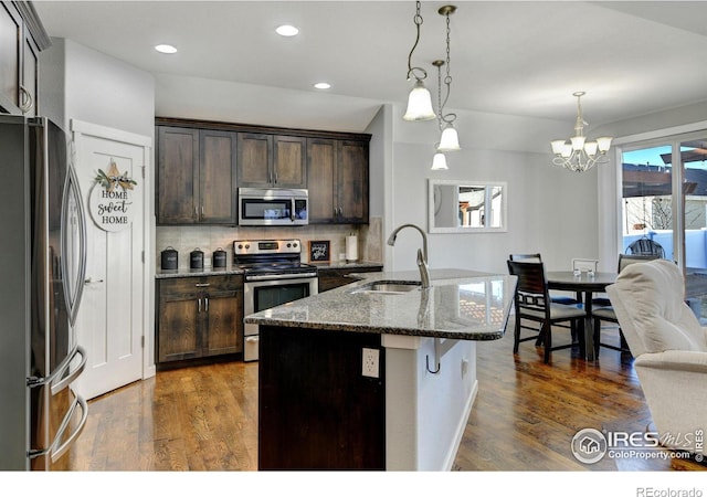 kitchen featuring sink, a center island with sink, hanging light fixtures, dark stone countertops, and stainless steel appliances