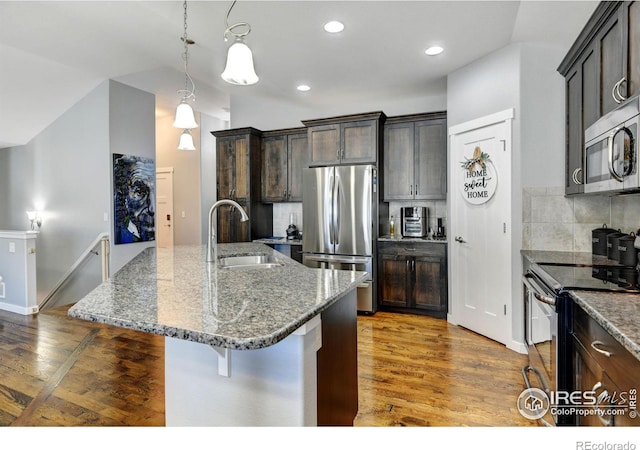 kitchen with sink, dark stone countertops, a breakfast bar area, stainless steel appliances, and a center island with sink