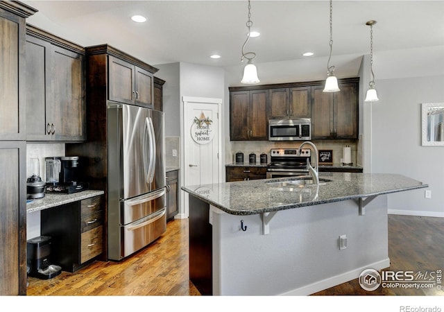 kitchen with decorative light fixtures, appliances with stainless steel finishes, dark brown cabinets, and dark stone counters