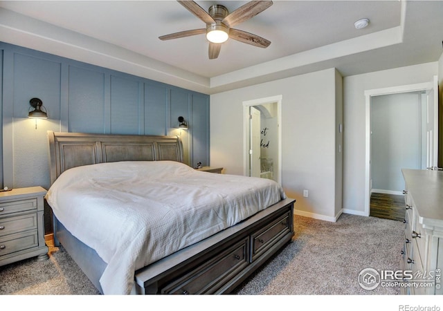 carpeted bedroom with ceiling fan, connected bathroom, and a raised ceiling