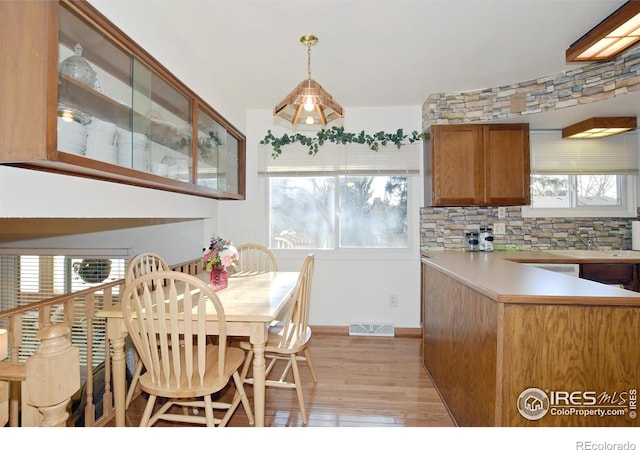 kitchen with sink, light wood-type flooring, hanging light fixtures, and tasteful backsplash