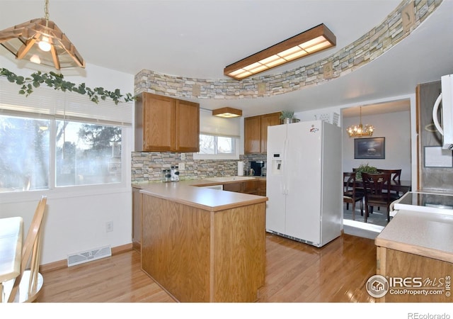 kitchen featuring white fridge with ice dispenser, hanging light fixtures, an inviting chandelier, backsplash, and light wood-type flooring