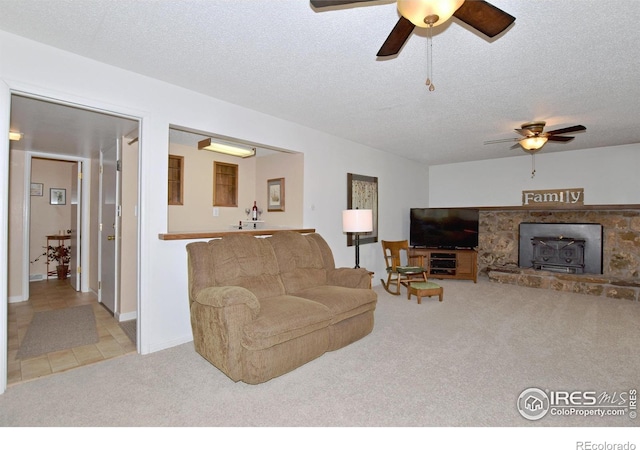 living room with ceiling fan, light colored carpet, a wood stove, and a textured ceiling