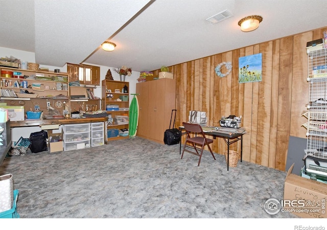 carpeted home office featuring wood walls and a textured ceiling