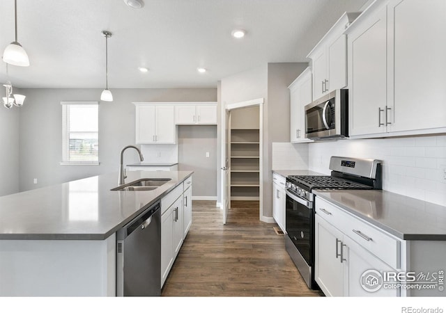 kitchen featuring appliances with stainless steel finishes, sink, decorative light fixtures, a center island with sink, and white cabinetry