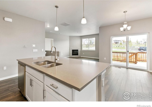 kitchen with sink, an island with sink, stainless steel dishwasher, and decorative light fixtures