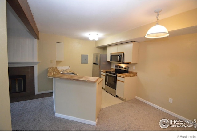 kitchen with pendant lighting, white cabinets, appliances with stainless steel finishes, kitchen peninsula, and a tiled fireplace