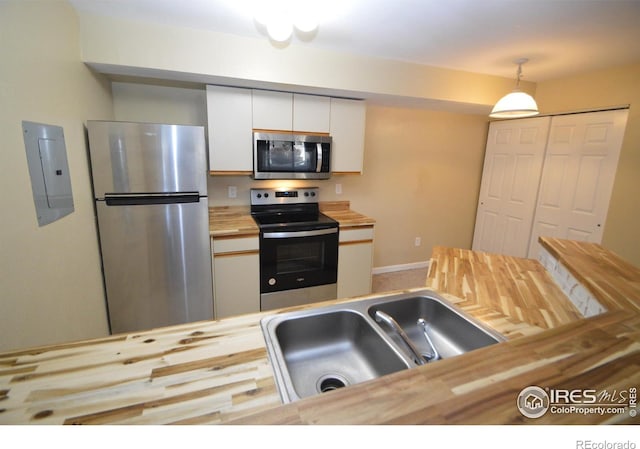 kitchen featuring stainless steel appliances, sink, white cabinets, butcher block countertops, and hanging light fixtures