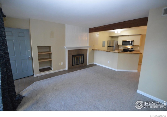 unfurnished living room with a tiled fireplace, light carpet, and beamed ceiling