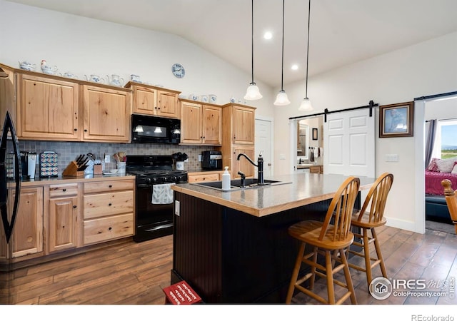 kitchen featuring an island with sink, sink, hanging light fixtures, black appliances, and a barn door