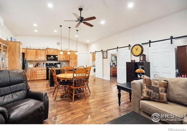 living room with ceiling fan, a barn door, high vaulted ceiling, and light wood-type flooring