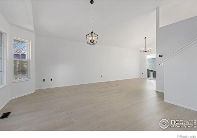 unfurnished living room with high vaulted ceiling, a notable chandelier, and light wood-type flooring