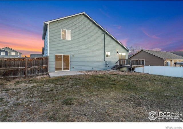 back house at dusk featuring a patio area, a deck, and a lawn