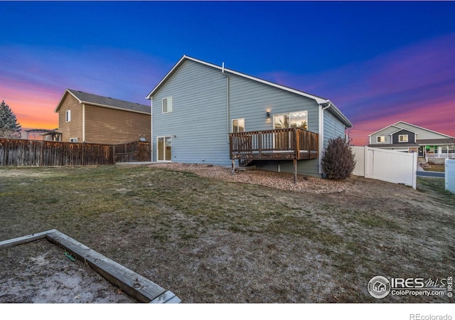 back house at dusk with a yard and a deck