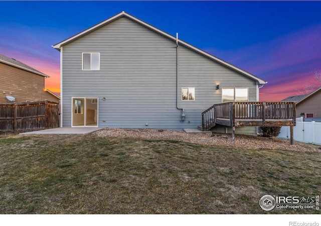 back house at dusk featuring a yard, a patio area, and a deck