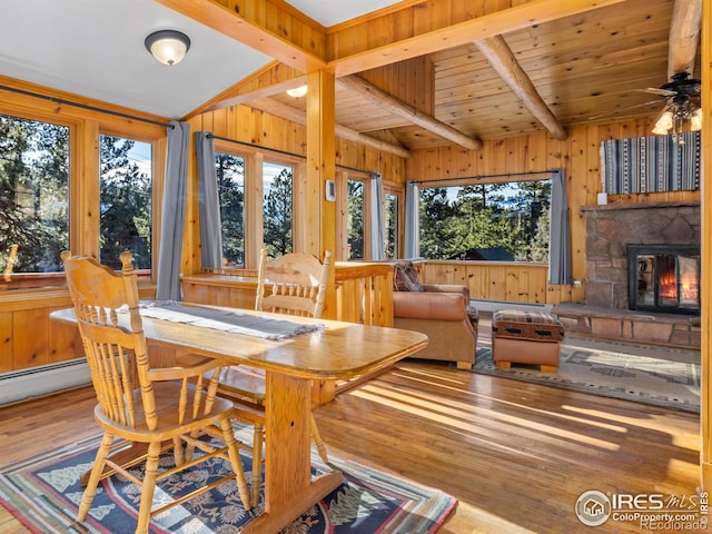 dining room with vaulted ceiling with beams, a stone fireplace, light wood-type flooring, and wooden walls