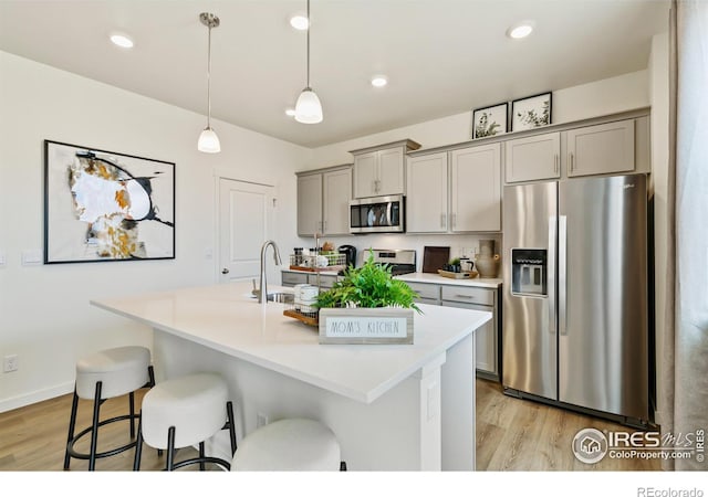 kitchen featuring gray cabinetry, stainless steel appliances, sink, light hardwood / wood-style floors, and an island with sink