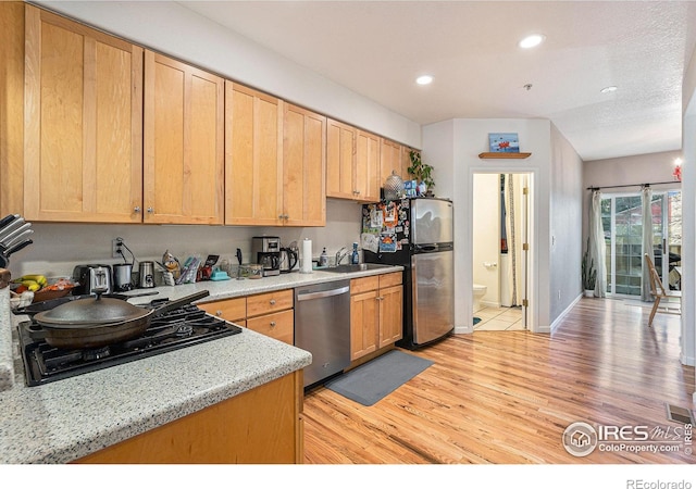 kitchen with light stone countertops, sink, light brown cabinets, stainless steel appliances, and light hardwood / wood-style floors