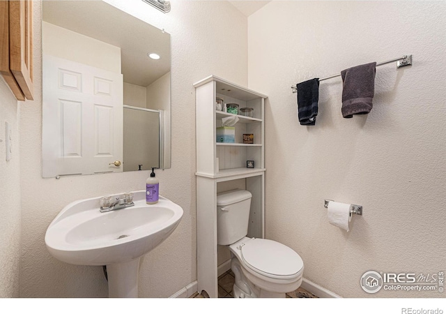 bathroom with sink, a shower with shower door, and toilet