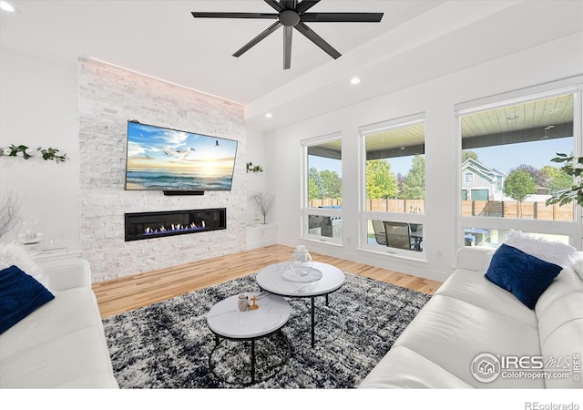 living room with hardwood / wood-style flooring, ceiling fan, and a stone fireplace