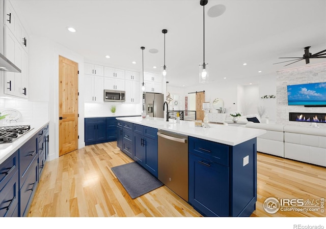 kitchen with blue cabinetry, light hardwood / wood-style flooring, a center island with sink, white cabinets, and appliances with stainless steel finishes