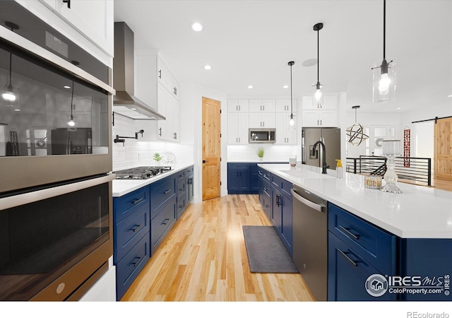 kitchen featuring a barn door, white cabinetry, blue cabinets, and wall chimney exhaust hood