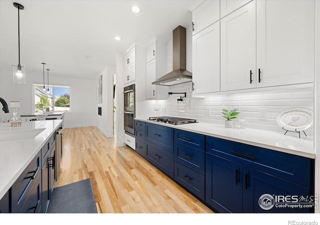 kitchen featuring white cabinets, sink, wall chimney range hood, and blue cabinets