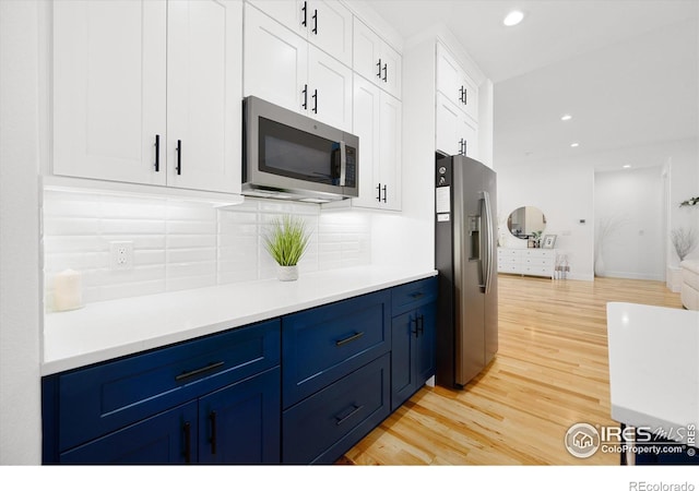 kitchen with white cabinetry, blue cabinets, appliances with stainless steel finishes, and light hardwood / wood-style flooring