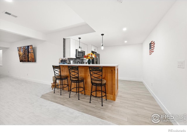 bar with pendant lighting, light wood-type flooring, tasteful backsplash, white cabinetry, and stainless steel appliances