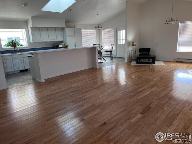 kitchen with decorative light fixtures, vaulted ceiling with skylight, a kitchen island, light hardwood / wood-style flooring, and sink