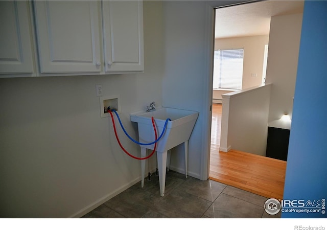 clothes washing area with dark tile patterned floors, washer hookup, cabinets, and baseboard heating