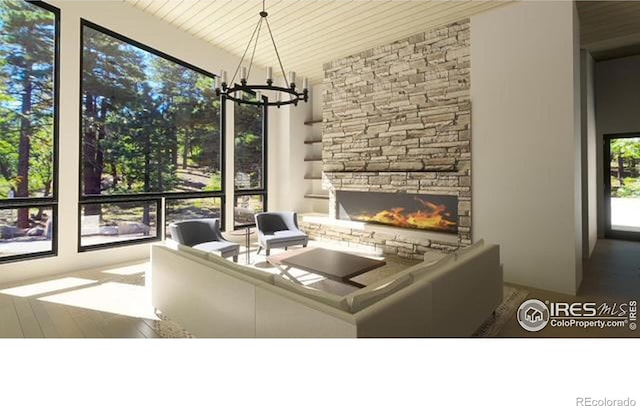 unfurnished living room with a healthy amount of sunlight, a stone fireplace, a notable chandelier, and wood-type flooring