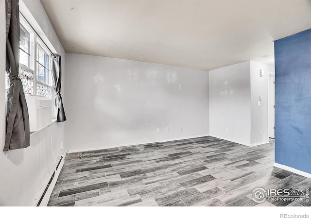 spare room featuring wood-type flooring and a baseboard heating unit