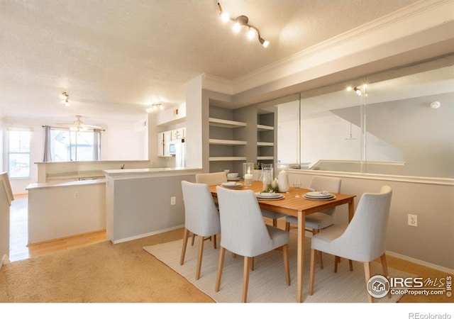 dining room with ceiling fan, built in shelves, ornamental molding, a textured ceiling, and light colored carpet