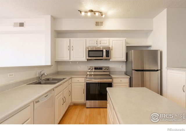 kitchen featuring appliances with stainless steel finishes, light wood-type flooring, a textured ceiling, sink, and white cabinetry