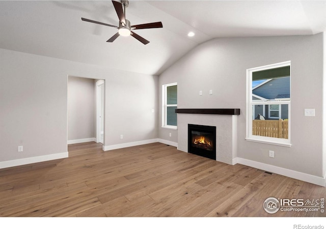 unfurnished living room with visible vents, vaulted ceiling, wood finished floors, and a glass covered fireplace