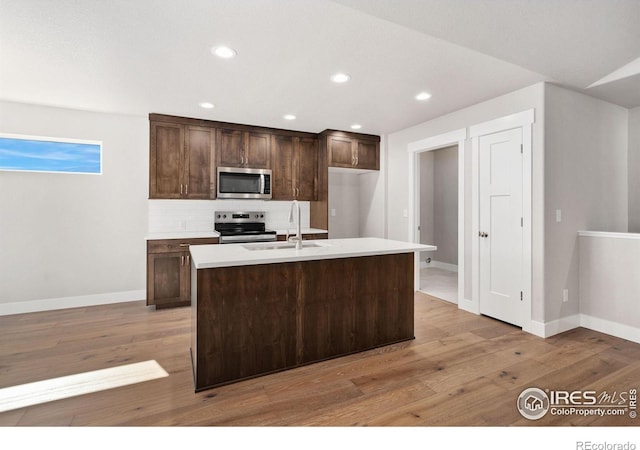 kitchen with decorative backsplash, appliances with stainless steel finishes, light wood-style floors, dark brown cabinetry, and a sink