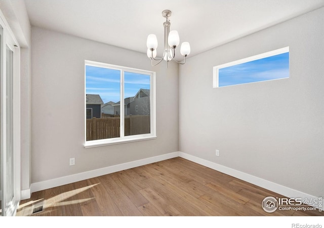 spare room featuring a chandelier, baseboards, wood finished floors, and a healthy amount of sunlight