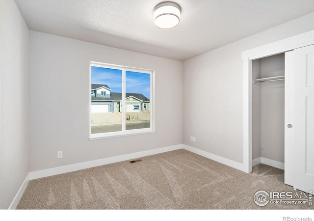 unfurnished bedroom with baseboards, visible vents, a textured ceiling, carpet flooring, and a closet