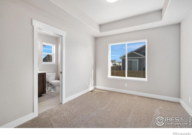 unfurnished bedroom with carpet floors, baseboards, and a raised ceiling