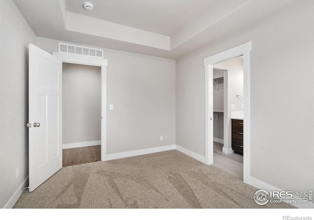 unfurnished bedroom featuring carpet, a raised ceiling, visible vents, and baseboards