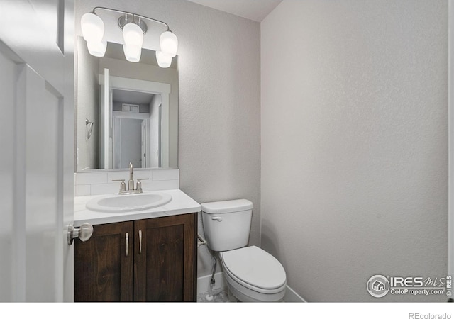 half bathroom with a textured wall, toilet, visible vents, vanity, and baseboards