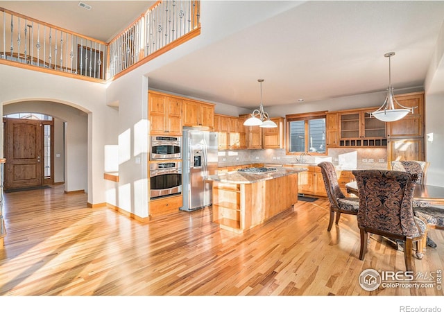 kitchen with decorative backsplash, appliances with stainless steel finishes, decorative light fixtures, light hardwood / wood-style floors, and a kitchen island