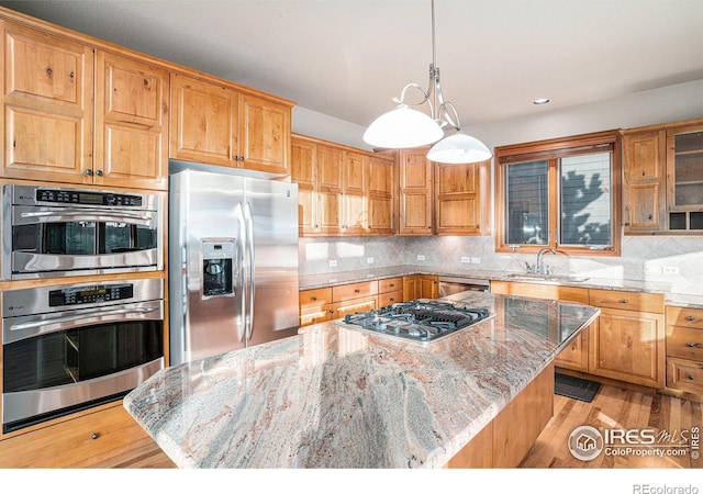 kitchen featuring light stone counters, stainless steel appliances, sink, light hardwood / wood-style flooring, and a kitchen island