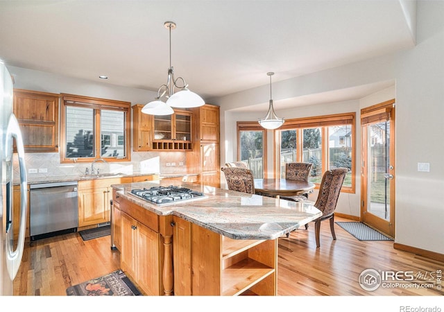 kitchen featuring light stone countertops, a center island, tasteful backsplash, light hardwood / wood-style floors, and appliances with stainless steel finishes