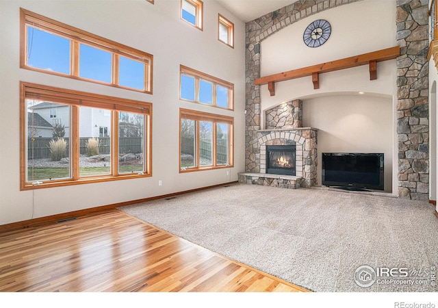 unfurnished living room featuring hardwood / wood-style flooring, beam ceiling, a fireplace, and a high ceiling