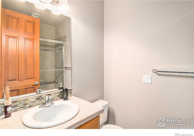 bathroom featuring vanity, backsplash, toilet, and a shower with shower door